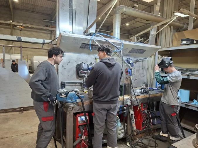Equipe d'apprentis chaudronniers de Métalinox échangeant autour d'un établi dans l'atelier de Mettray
