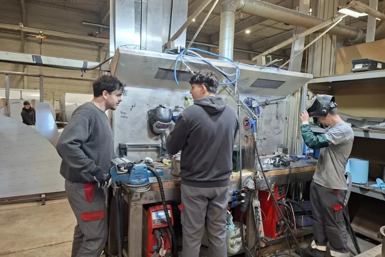 Equipe d'apprentis chaudronniers de Métalinox échangeant autour d'un établi dans l'atelier de Mettray